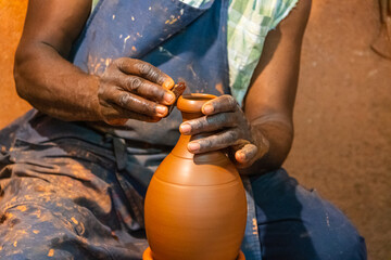Gros plan sur les mains d'un homme de couleur noir qui fabrique une poterie en argile.	