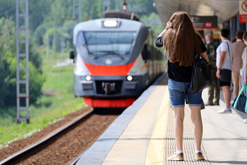 People waiting for the arriving train on railroad station. Commuter train passengers at summer