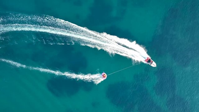 Tubing boat with people moving behind the boat on the water. Aerial view of motor speed boat pulls inflatable rubber raft with people. Summer vacation shot
