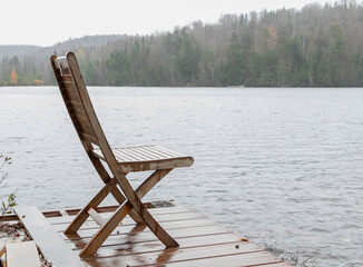 chaise en bois au bord d'un lac avec une forêt en arrière plan lors d'une journée brumeuse