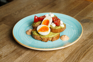 Avocado toast with guacamole, soft boiled egg, cream cheese and tomatoes on a plate