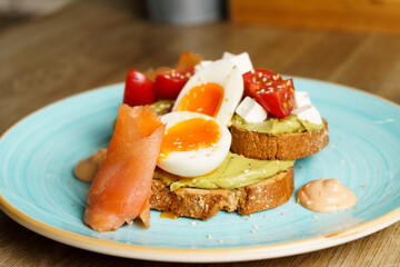 Avocado toast with guacamole, soft boiled egg, salmon, cream cheese and tomatoes on a plate