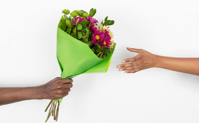 Hand of young african american guy gives bouquet of flowers to woman