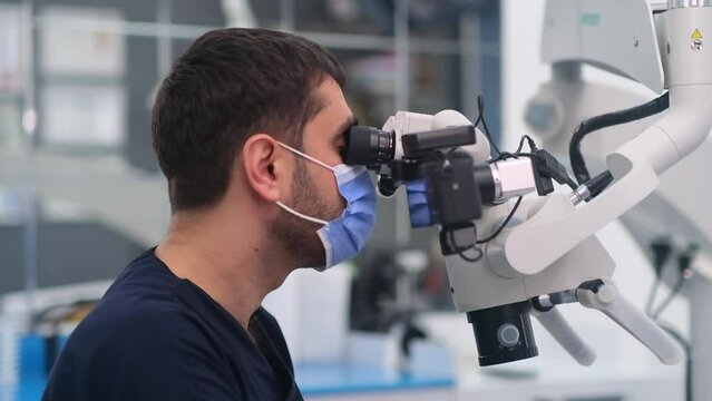 Bearded doctor looking in modern dental microscope to check cavity of patient on couch focused dentist using innovative technology for checkup in dentistry clinic