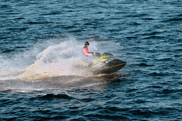 A girl of 20-30 years old is sailing on a jet ski on the sea. A young woman floats on a watercraft at high speed on the water, splashing to the sides.