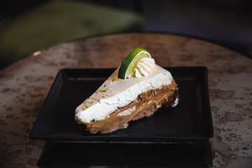 Lime slice decorated lemon cheesecake on black plate. 