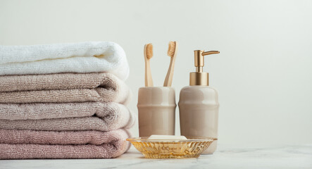 Vintage golden bath supplies with stack of clean soft towels next to soap and toothbrushes. White,...