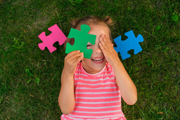 A ludicrous child is playing with puzzles while lying on the lawn grass. Children's toys for the...
