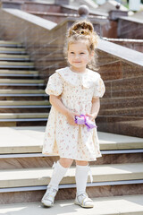Cute little girl standing on the steps in a park and holding a little pony in hand