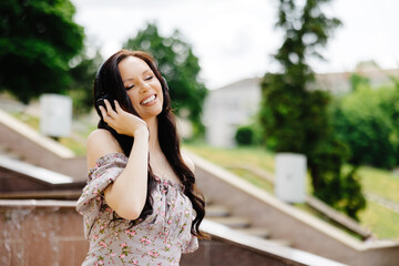 Fototapeta premium Dancing girl feeling happy in city.Young woman dancing and listening music in headphones, standing on the stairs in park