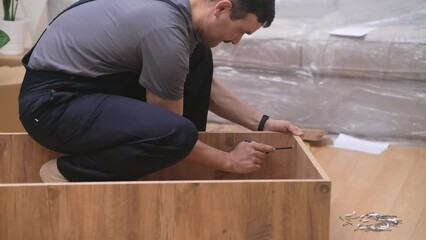 Furniture made of quality wood materials assembling process carpenter in coveralls screwing nails into wooden rack using professional instruments carpentry industry