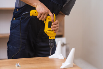 Professional furniture assembling and fixing employee attaching legs to wooden cabinet with...