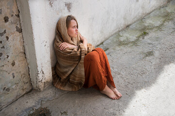 A girl in poor clothes sits on the ground