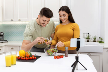 Beautiful young family husband and wife cooking together, using smartphone