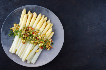 Traditional Bavarian white asparagus with wild garlic- and almond butter served as top view on a Nordic Design plate with text space right