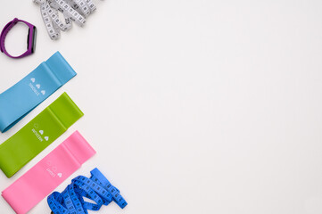 Layout of fitness rubber bands with different levels of resistance, measuring tapes, fitness bracelet on white, top view