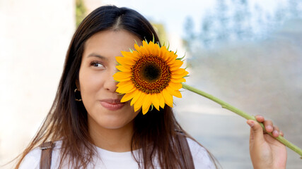mujer joven, sonriendo y sosteniendo un girasol en un día soleado de primavera en un parque,...