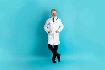 Positive friendly mature doctor posing on blue background