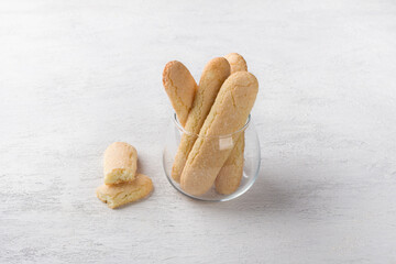 Freshly baked homemade savoiardi cookies in a glass cup on a light gray table