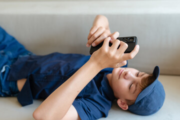 Teenager boy using smart phone on sofa living room at home. Boy holding and using cellphone for searching data and social media on internet. Teenager and Technology concept. Communication with friends