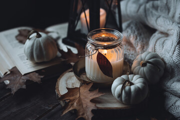 Autumn home composition with aromatic candle, pumpkin, wool sweater. Aromatherapy on a grey fall morning, atmosphere of cosiness and relax. Wooden dark background