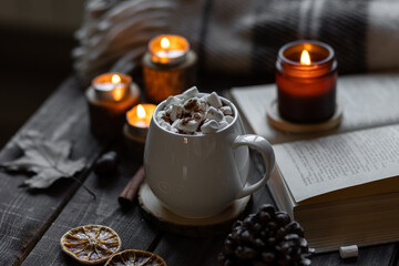 Aromatherapy on a grey fall morning, atmosphere of cosiness and relax. Wooden background, books, close up. Autumn cozy home composition with hot chocolate with marshmallow and candles. 