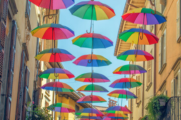 Fototapeta na wymiar Rainbow umbrellas on blue sky background. Many colorful umbrellas, street decoration for festivals. Concept diversity