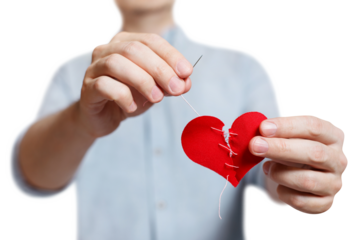 Hands repairing a broken red heart using needle and thread, cut out