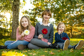Fototapeta na wymiar Two big sisters and their toddler brother having fun outdoors. Two young girls with a toddler boy on autumn day. Children with large age gap. Big age difference between siblings.