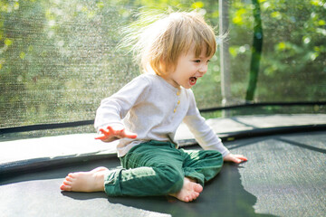 Cute toddler boy jumping on a trampoline in a backyard on warm and sunny summer day. Sports and exercises for children. Summer outdoor activities.