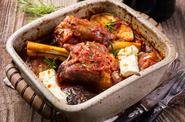 Traditional Greek braised lamb knuckle with feta cheese and eggplant in spicy tomato sauce served...