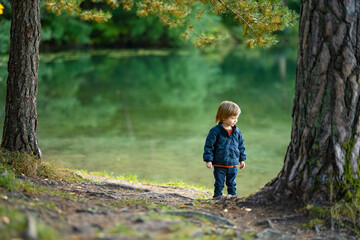 Adorable toddler boy admiring the Balsys lake, one of six Green Lakes, located in Verkiai Regional Park. Child exploring nature on autumn day in Vilnius, Lithuania.