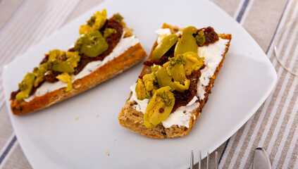 Top view of yummy sandwich with cheese, sun-dried tomatoes olives on the white plate with on the tablecloth in cafeteria