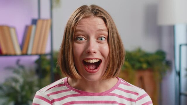Oh my God, Wow. Brunette young woman surprised looking at camera with big eyes, shocked by sudden victory, good win news, celebrating at home. Excited amazed girl indoors in living room on couch