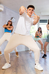 Group of young women and young guy in sunglasses rehearsing hip hop dance in dance studio