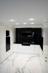 CHICAGO, IL, USA 2022 A luxurious, modern kitchen with white and black cabinets, gold hardware faucets, and white herringbone marble tiles.