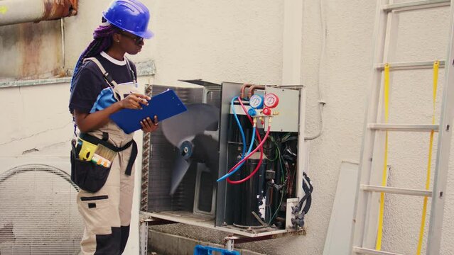 Professional wireman commissioned for external air conditioner routine check up, writing findings on clipboard. Specialist doing hvac system investigation of damaged parts