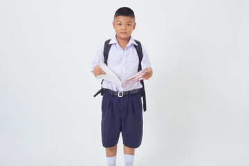 A young Asian cute boy standing in a Thai school uniform with a backpack bag and book on a white background banner