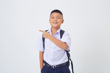A young Asian cute boy standing in a Thai school uniform with a backpack bag and book on a white...