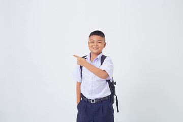 A young Asian cute boy standing in a Thai school uniform with a backpack bag and book on a white background banner