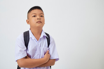 A young Asian cute boy standing in a Thai school uniform with a backpack bag and book on a white background banner