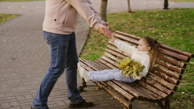 Happy family, dad, little daughter, walk together in park, autumn. Father, child collect yellow maple leaves for walk. Happy childhood, fatherhood. Girl plays, hugs dad on street. Family relationships