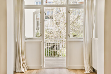 an empty room with white curtains on the windows and wooden floor in front of the window there is a tree outside view