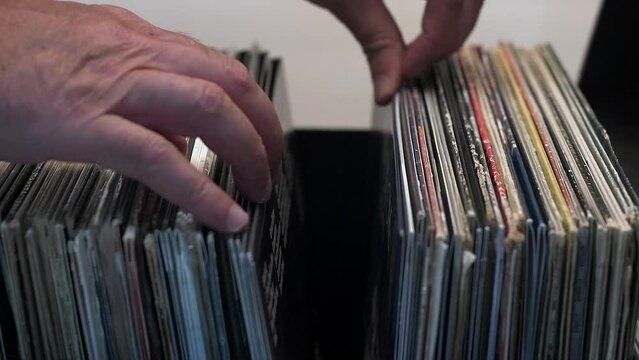 male music lover flips through a stack of vinyl records in a music store. Close-up.