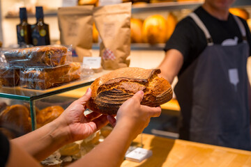 Customer hands in the bakery shop buying a loaf from the baker in the workshop workshop