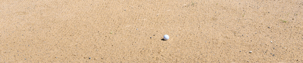 Golf ball in a freshly groomed sand trap, recreation and challenge on a sunny summer day
