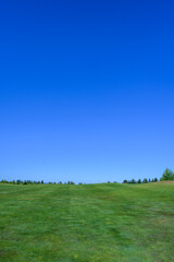 Relaxing day on the golf course, fairway grass running up to clear blue sky, recreation and challenge on a sunny summer day
