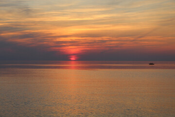 Naklejka na ściany i meble Sunset at the Baltic Sea in Saulkrasti, Lativa with a small boat on the horizon