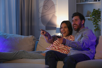 Happy couple watching TV on sofa at home, space for text