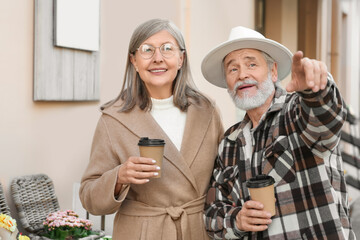 Affectionate senior couple drinking coffee outdoors, space for text